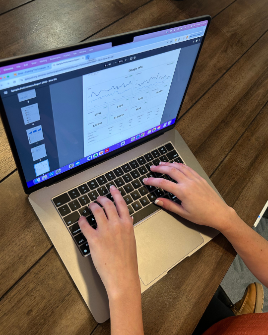 An overhead view of a PTE employee working on their computer, assessing a chart with Google Pay-Per-Click performance charts