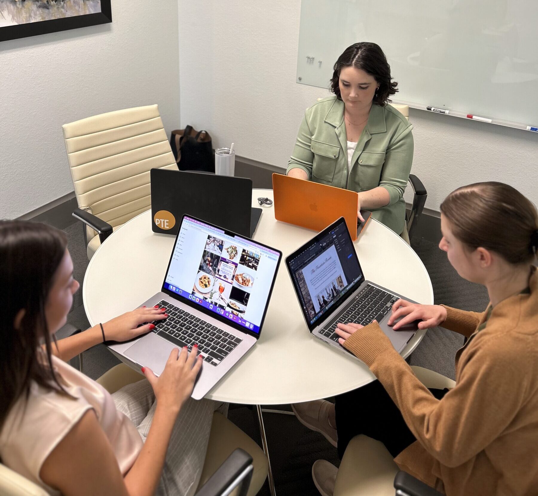 PTE team members (3 women) working at a circular table on their laptops